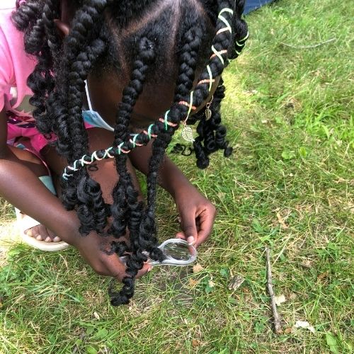Child using a hand lens to look at something in the grass