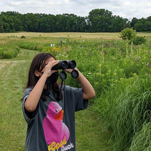 Child standing in a prairie looking through binoculars.