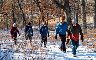 Five adults walking along a snowy trail with oak trees in the background