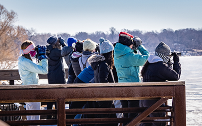 A group of youth with binoculars on a bridge looking out at a frozen lake