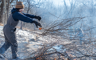 A youth participant throwing brush into a fire with snow dotting the landscape